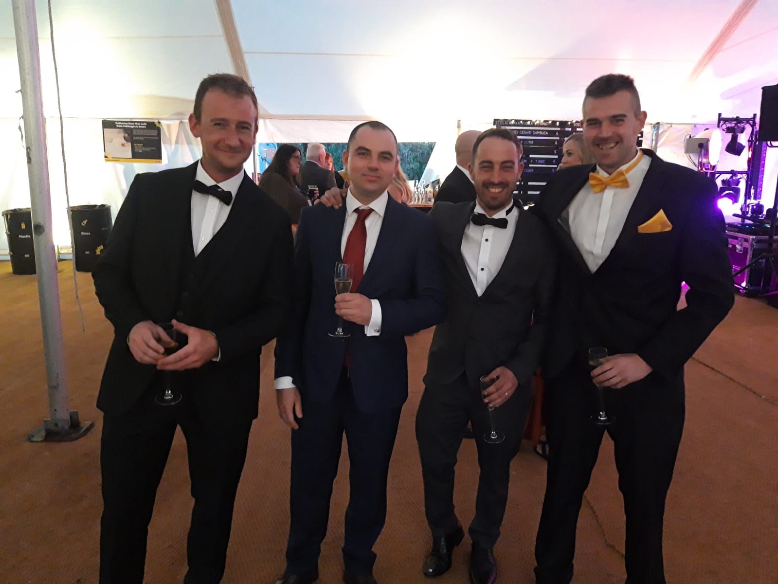 A photo of four gentlemen in suits stood in a line taking a event photo.